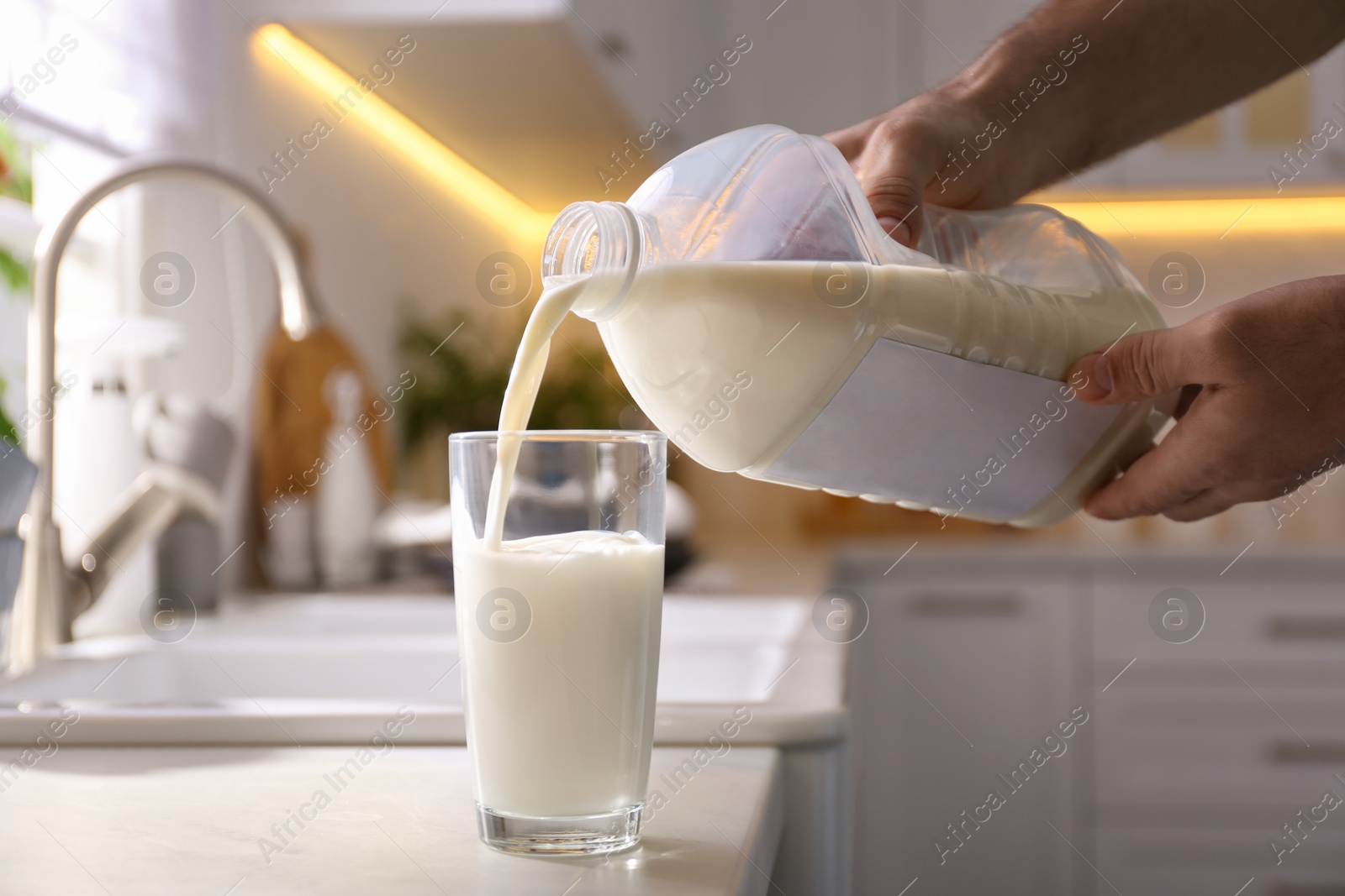 Photo of Man pouring milk from gallon bottle into glass at white countertop in kitchen, closeup