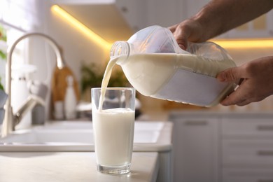 Photo of Man pouring milk from gallon bottle into glass at white countertop in kitchen, closeup