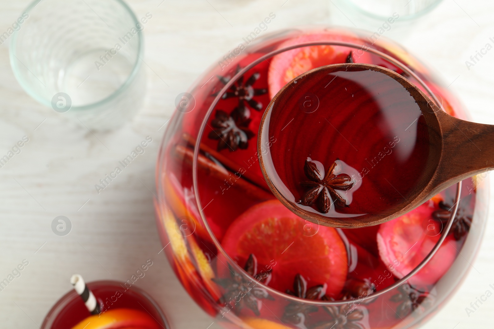 Photo of Ladle of delicious aromatic punch drink over bowl on white wooden table, top view