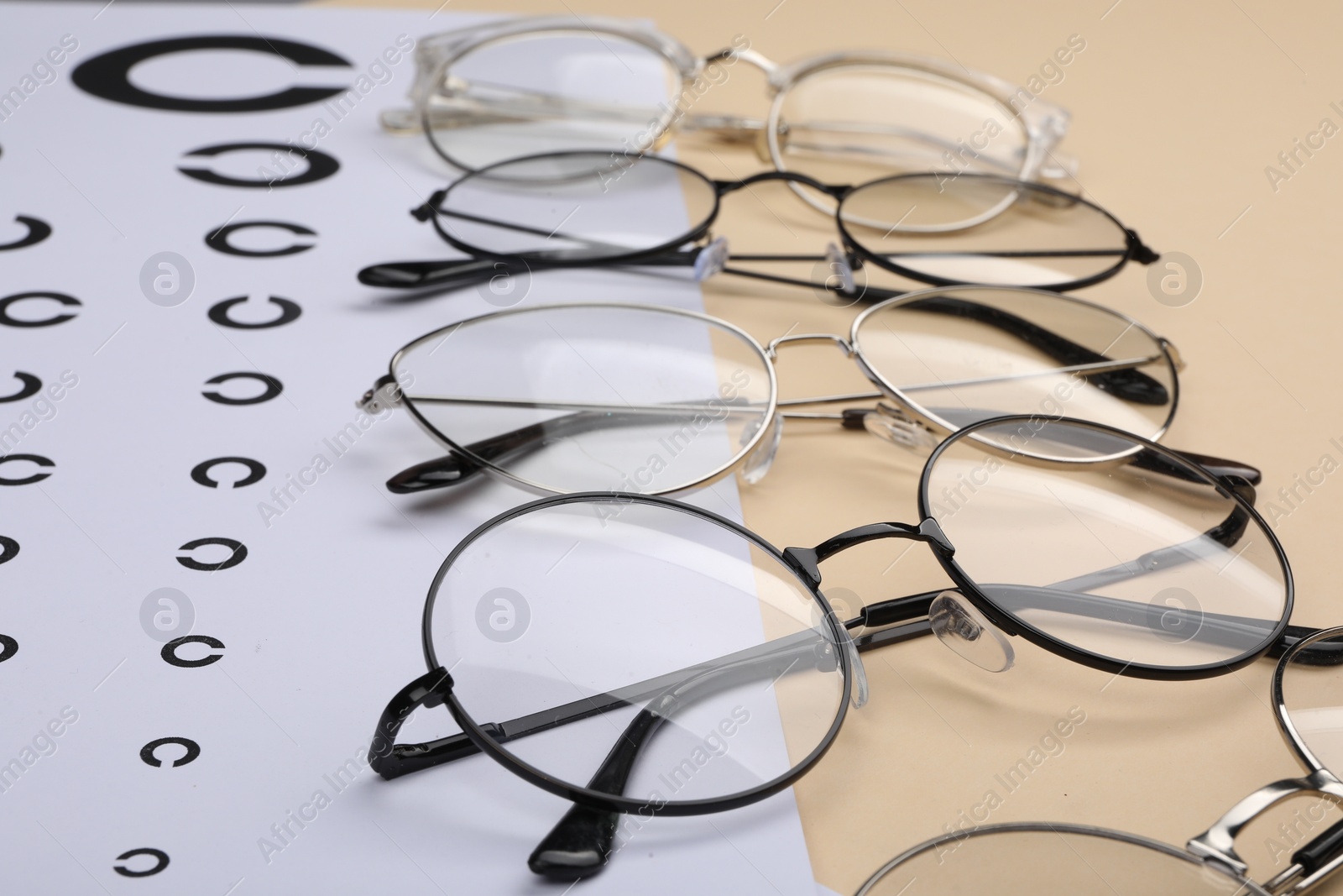 Photo of Vision test chart and glasses on beige background, closeup