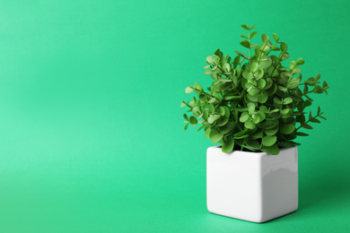 Beautiful artificial plant in flower pot on green background, space for text