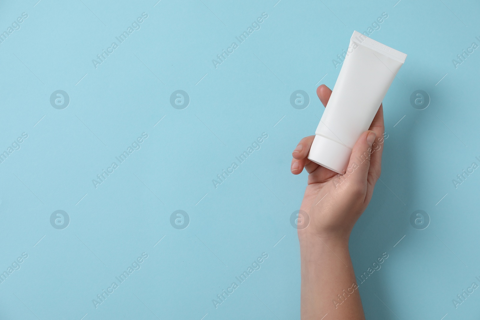 Photo of Woman with tube of hand cream on light blue background, top view. Space for text