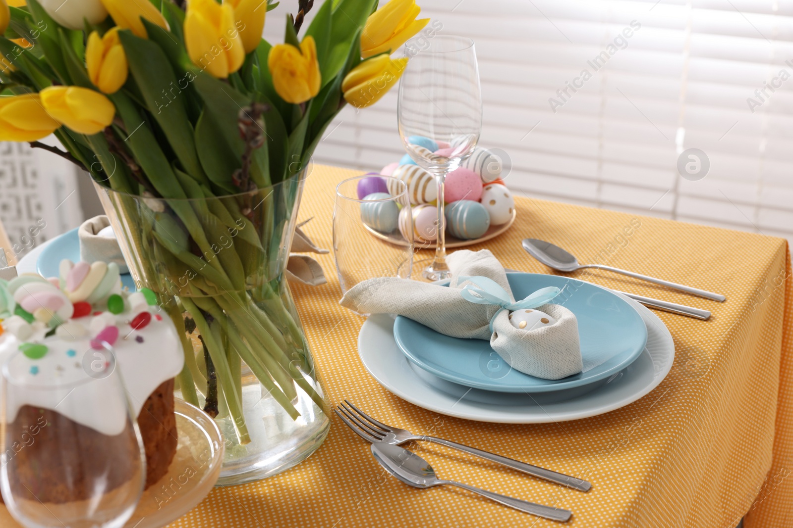 Photo of Festive table setting with painted eggs, cutlery and vase of tulips. Easter celebration