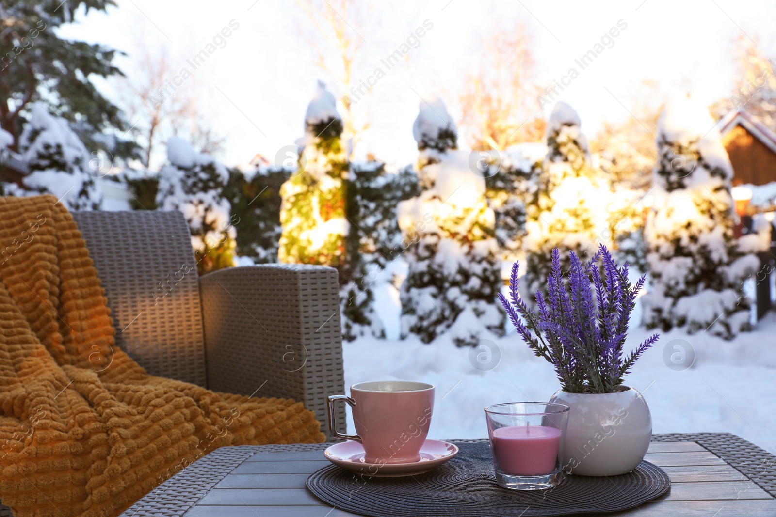 Photo of Candle, potted flowers and cup of hot drink on coffee table outdoors. Cosy winter