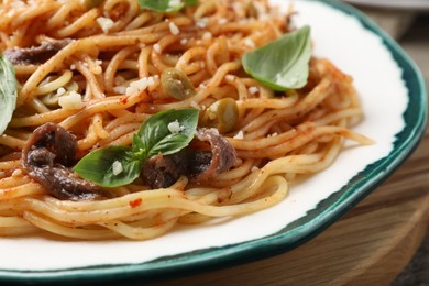 Photo of Delicious pasta with anchovies, tomato sauce and basil on plate, closeup