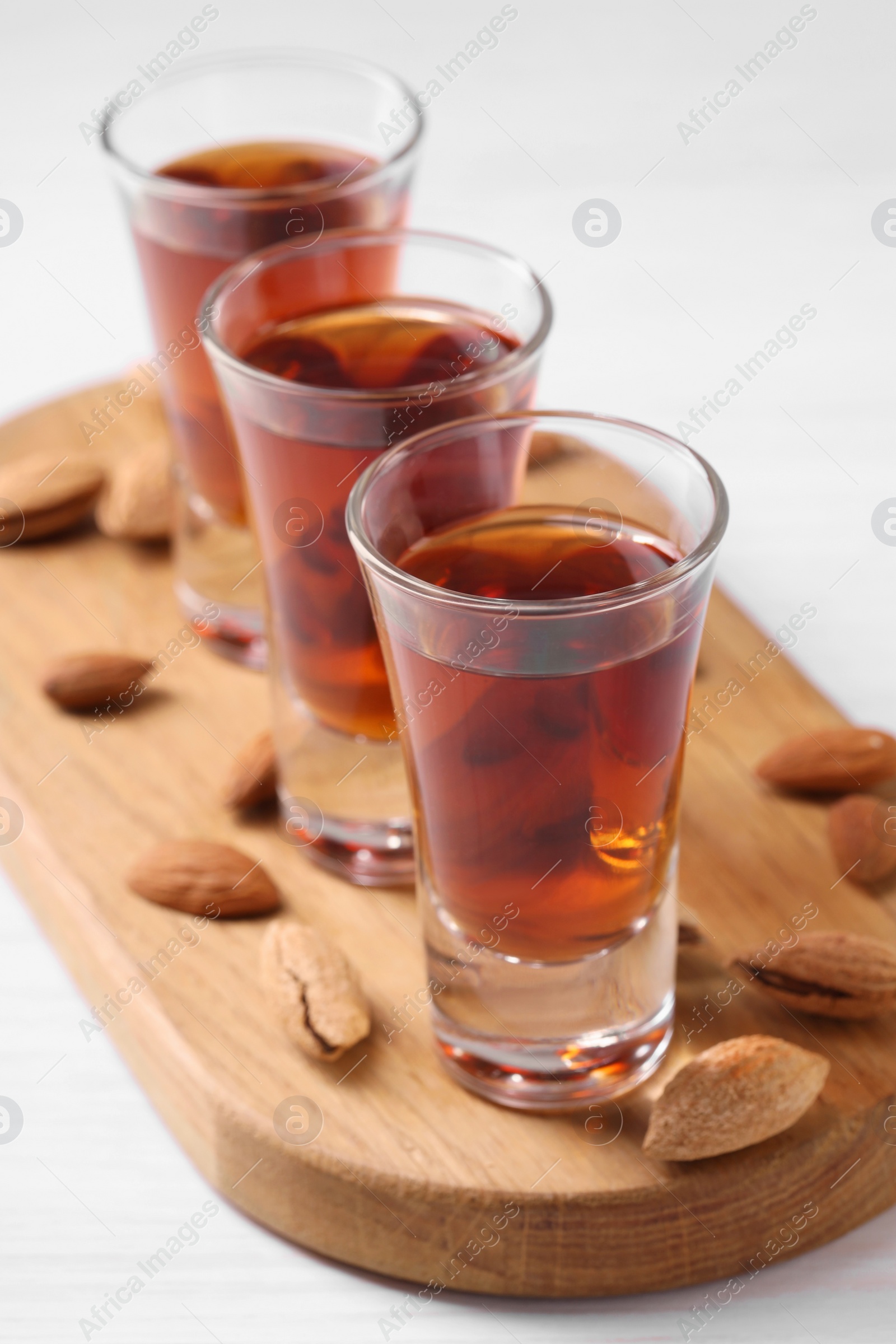 Photo of Shot glasses with tasty amaretto liqueur and almonds on white wooden table, closeup