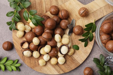 Photo of Tasty Macadamia nuts and green twigs on grey table, flat lay