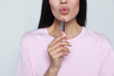 Young woman with beautiful makeup holding nude lipstick on light gray background, closeup