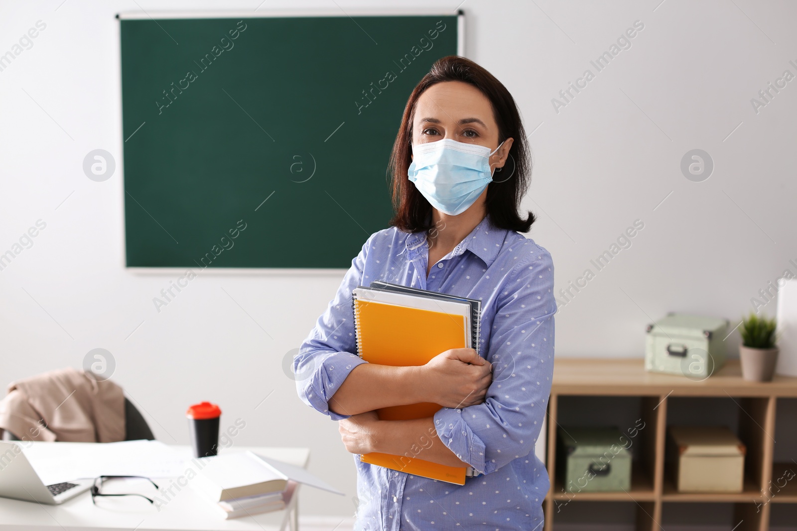 Photo of Teacher with protective mask and copybooks in classroom. Reopening after Covid-19 quarantine