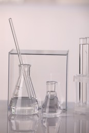 Photo of Laboratory analysis. Glass flasks and stirring rod on white table against blurred background