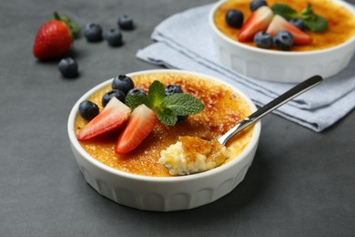 Photo of Delicious creme brulee with berries in bowl and spoon on grey table, closeup