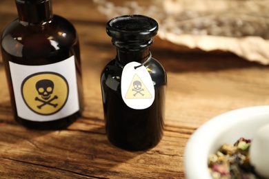 Photo of Open glass bottle of poison with warning sign on wooden table, closeup