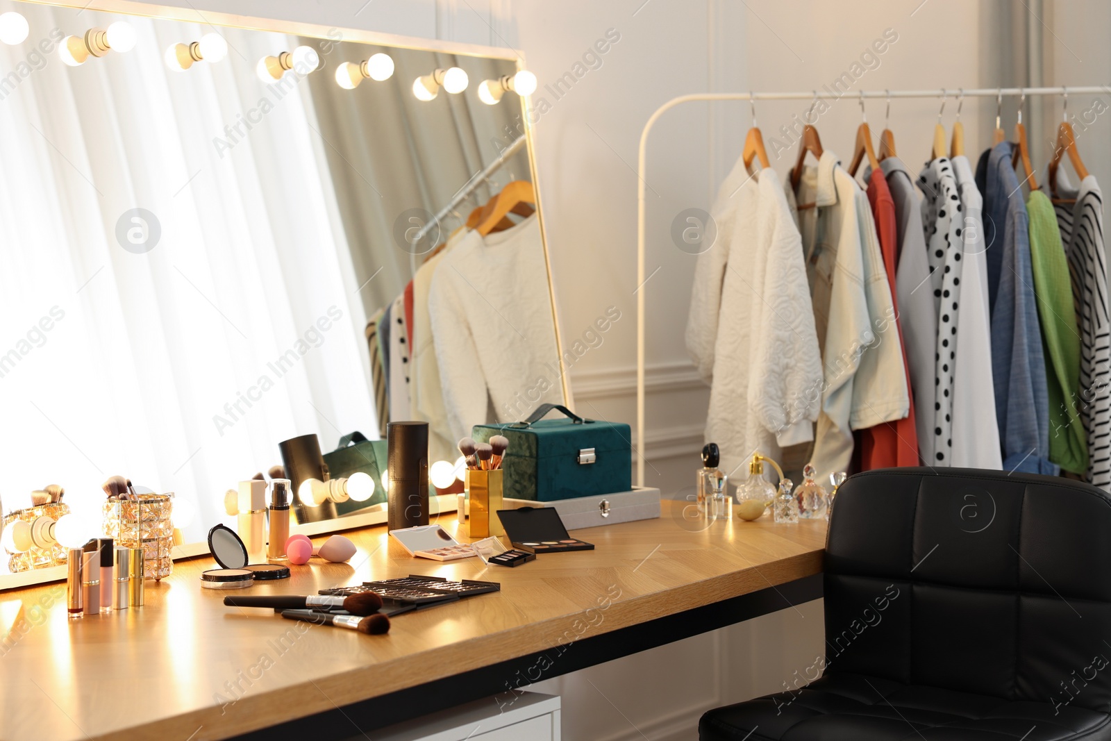 Photo of Makeup room. Stylish dressing table with mirror, chair and clothes rack