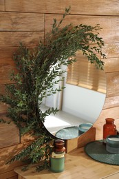 Stylish mirror decorated with green eucalyptus on wooden wall in room