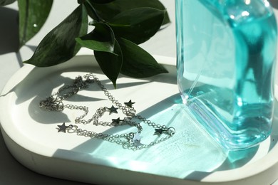 Metal chain with pendants, perfume and green leaves on table, closeup. Luxury jewelry