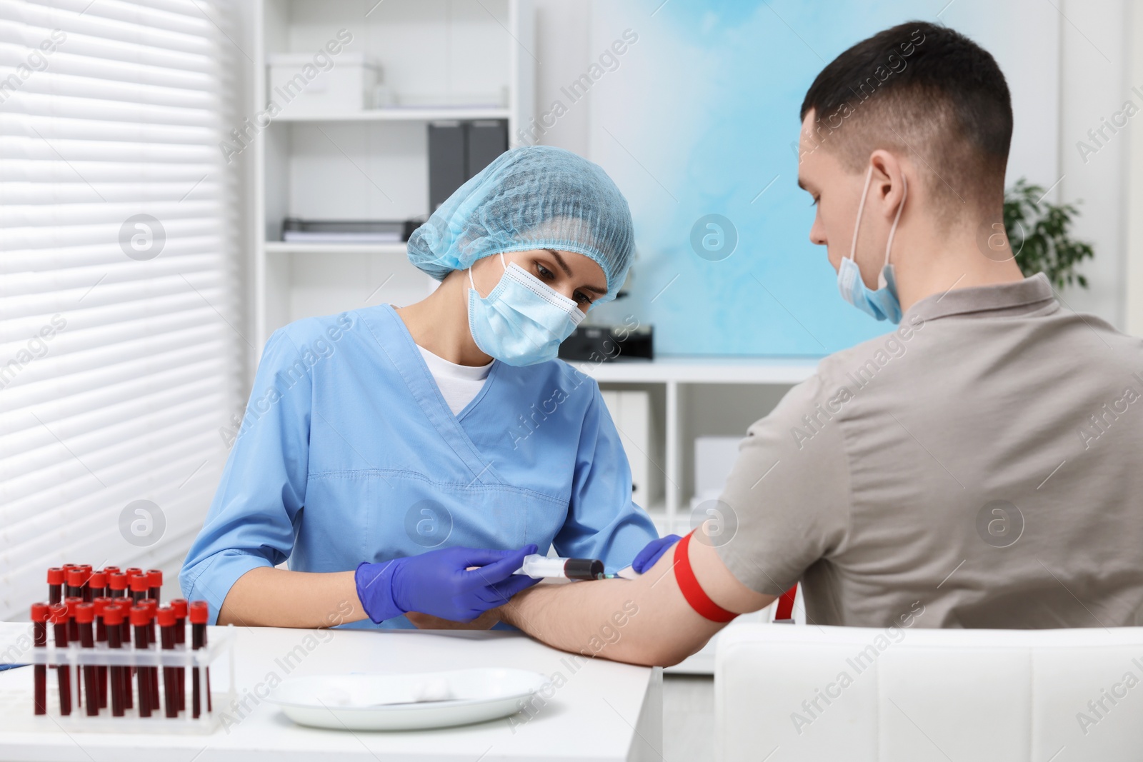 Photo of Laboratory testing. Doctor taking blood sample from patient at white table in hospital