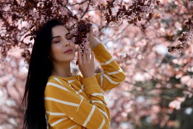 Pretty young woman near beautiful blossoming trees outdoors. Stylish spring look