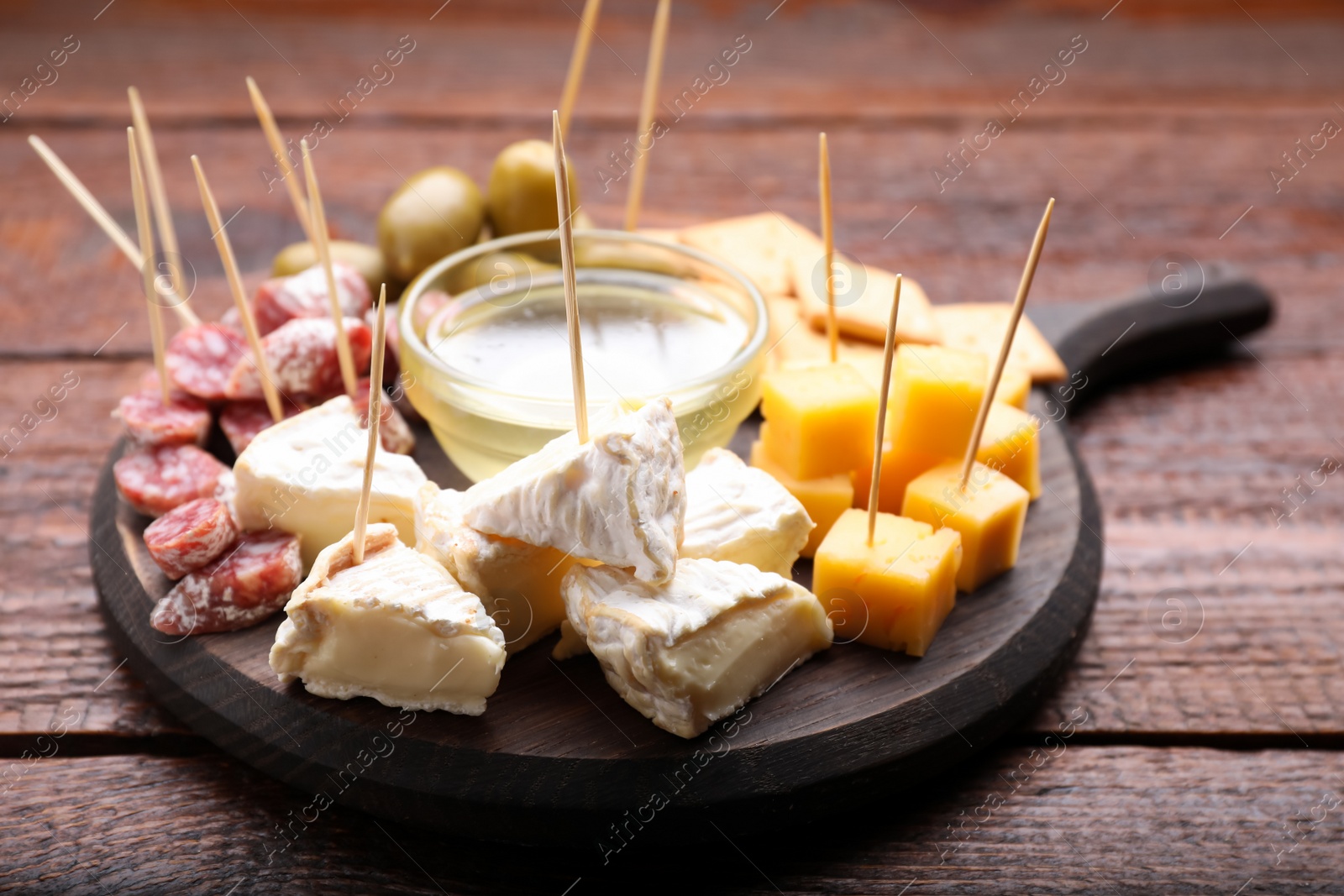 Photo of Toothpick appetizers. Pieces of cheese, sausage and honey on wooden table, closeup
