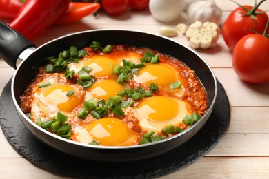 Photo of Delicious shakshuka in frying pan on light wooden table, closeup