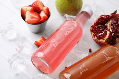 Photo of Tasty kombucha in glass bottles, fresh fruits and ice on white table, closeup