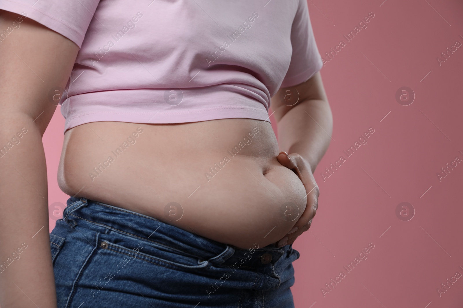 Photo of Woman touching belly fat on pink background, closeup. Overweight problem