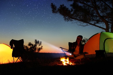 Photo of Woman with flashlight near bonfire at night. Camping season