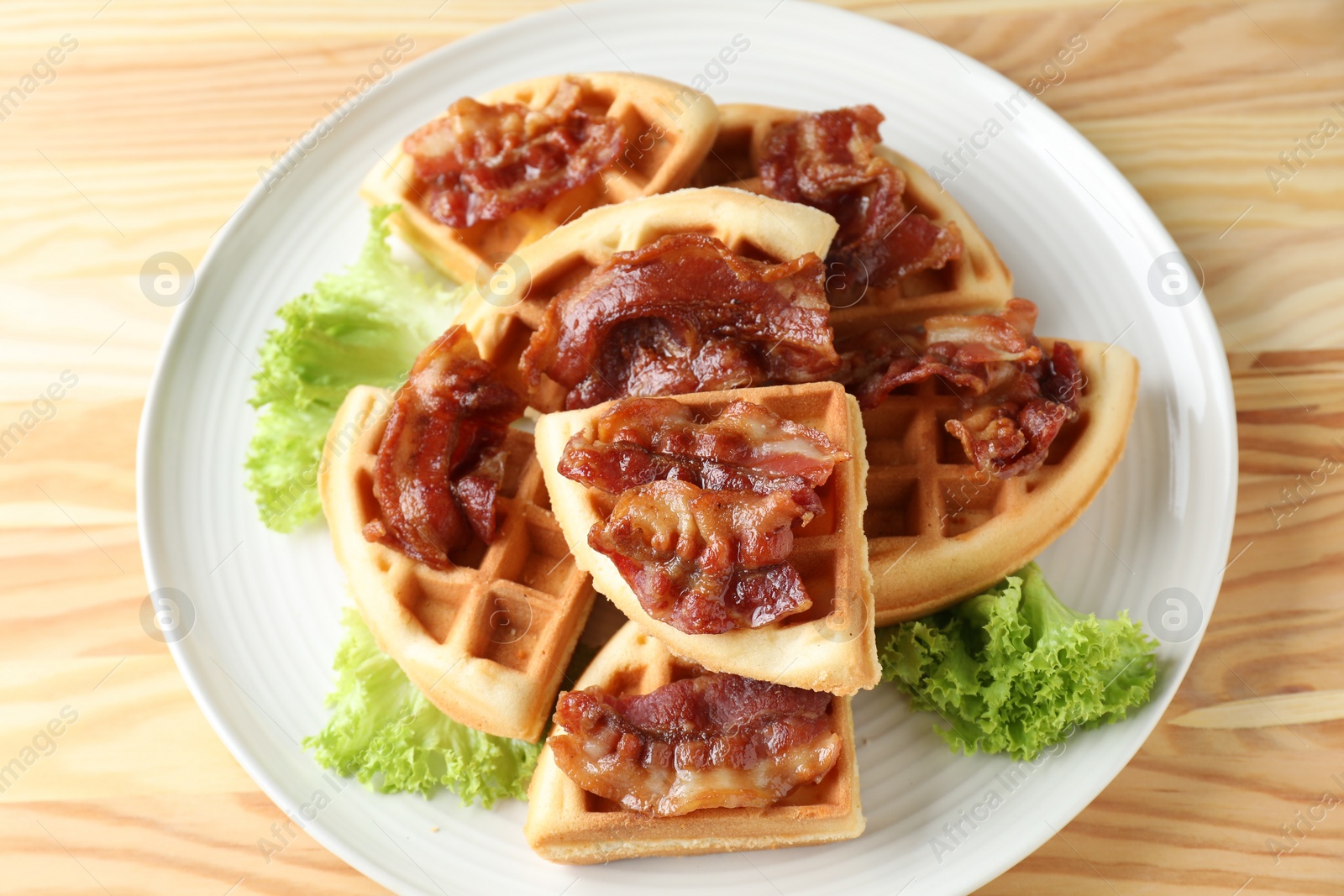 Photo of Tasty Belgian waffles served with bacon and lettuce on wooden table, closeup