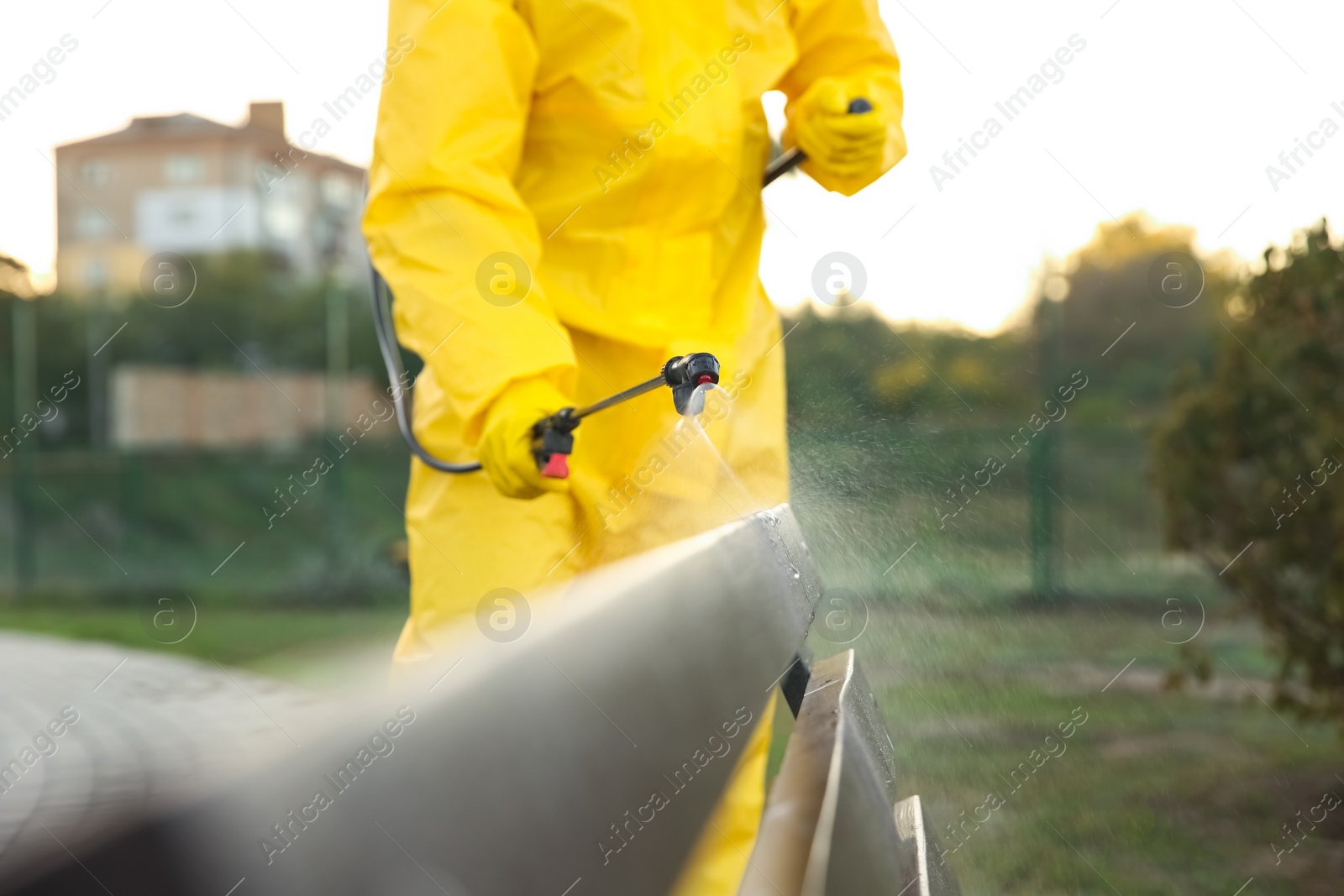 Photo of Person in hazmat suit disinfecting bench in park with sprayer, closeup. Surface treatment during coronavirus pandemic