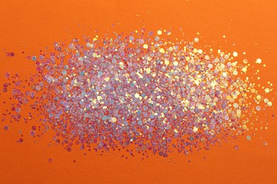 Photo of Shiny bright lilac glitter on orange background, flat lay