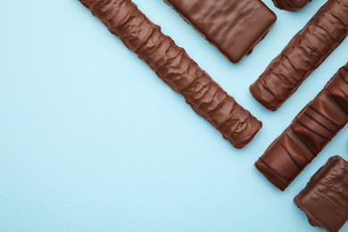 Different tasty chocolate bars on light blue background, flat lay. Space for text