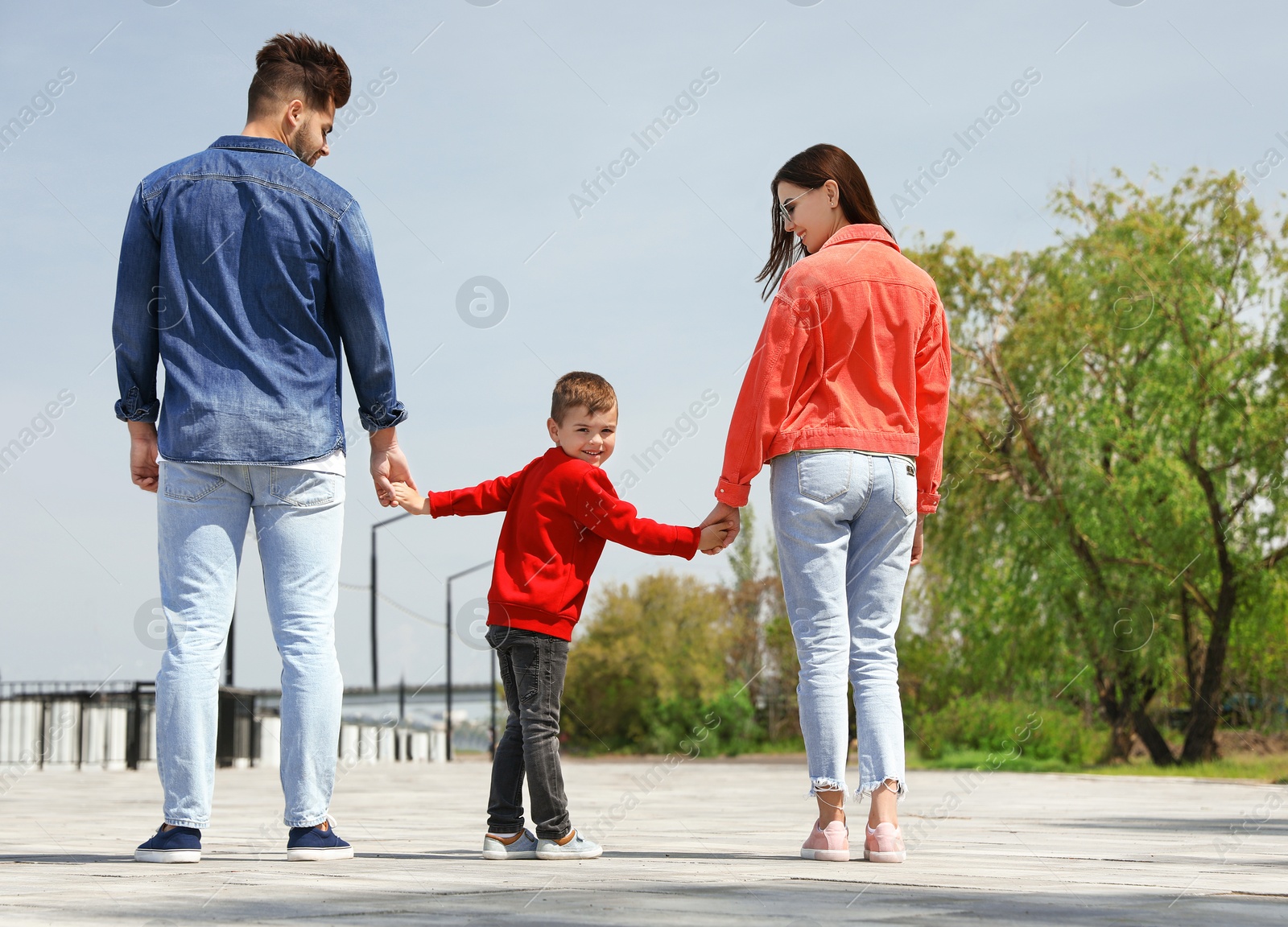 Photo of Happy child holding hands with his parents outdoors. Family weekend