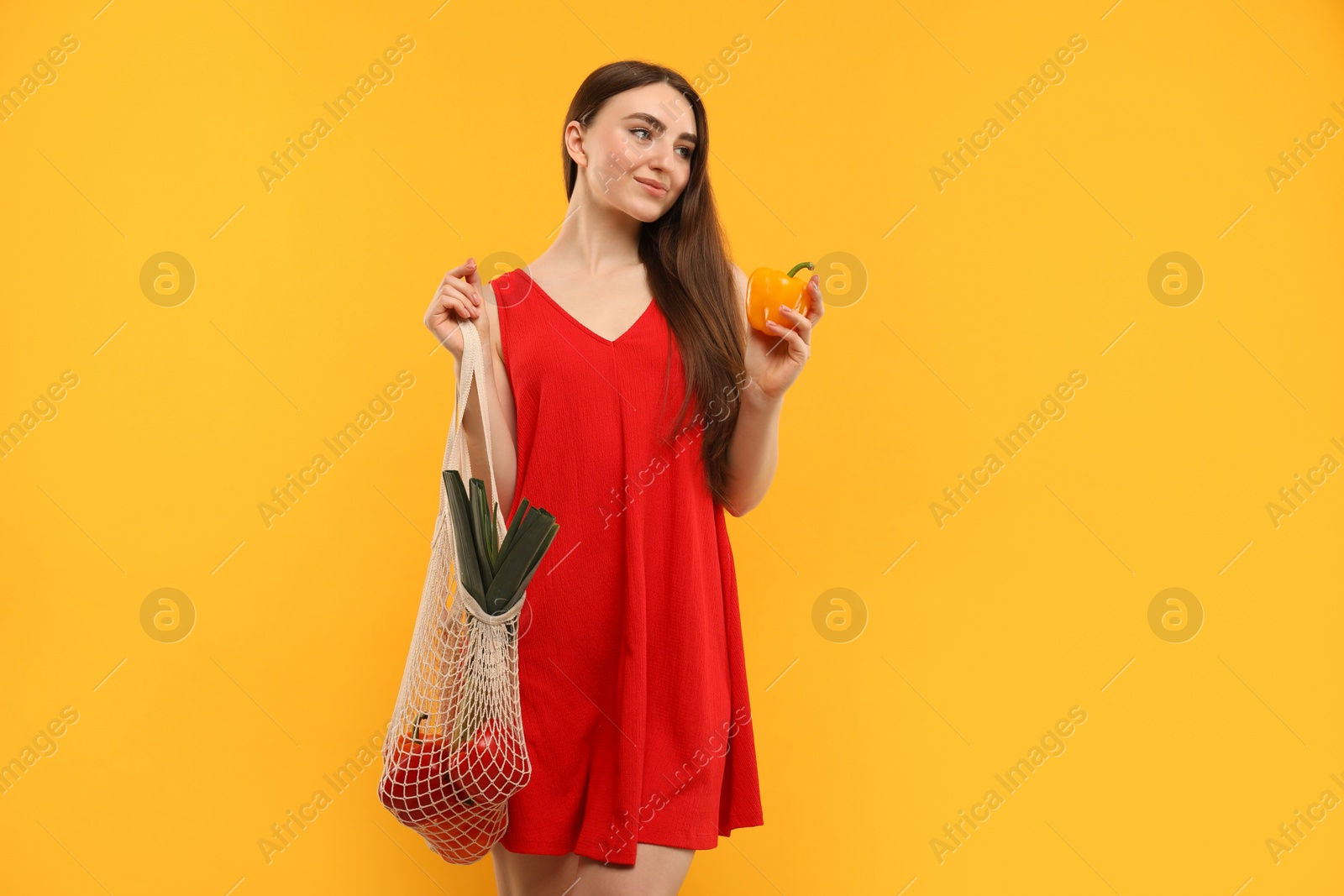 Photo of Woman with string bag of fresh vegetables on orange background