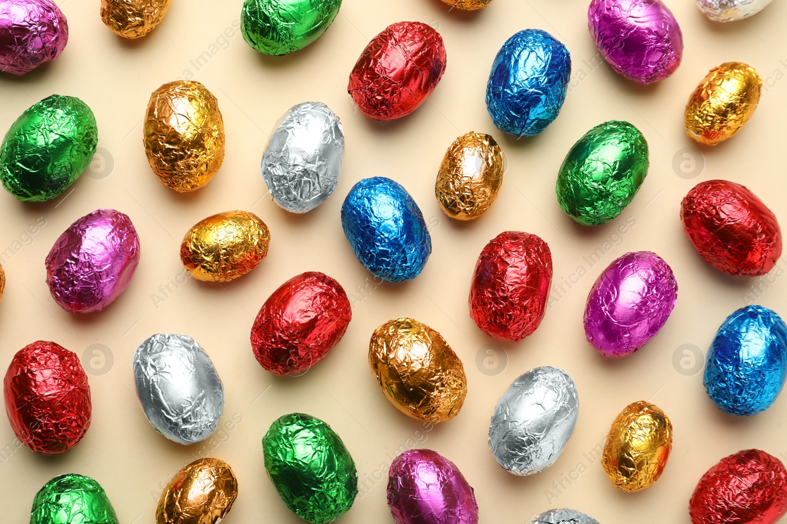 Photo of Chocolate eggs wrapped in colorful foil on beige background, flat lay