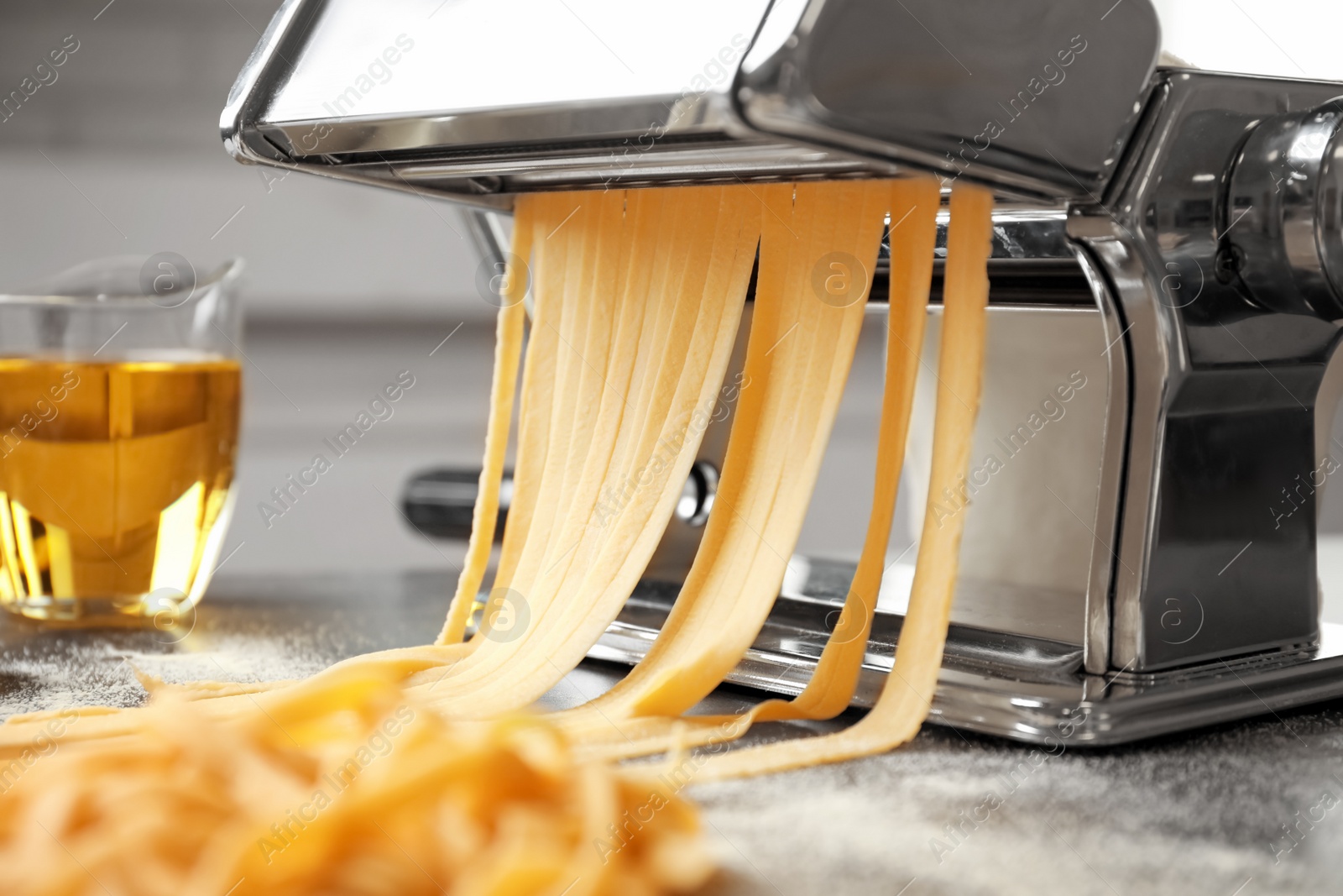 Photo of Pasta maker with dough and oil on kitchen table