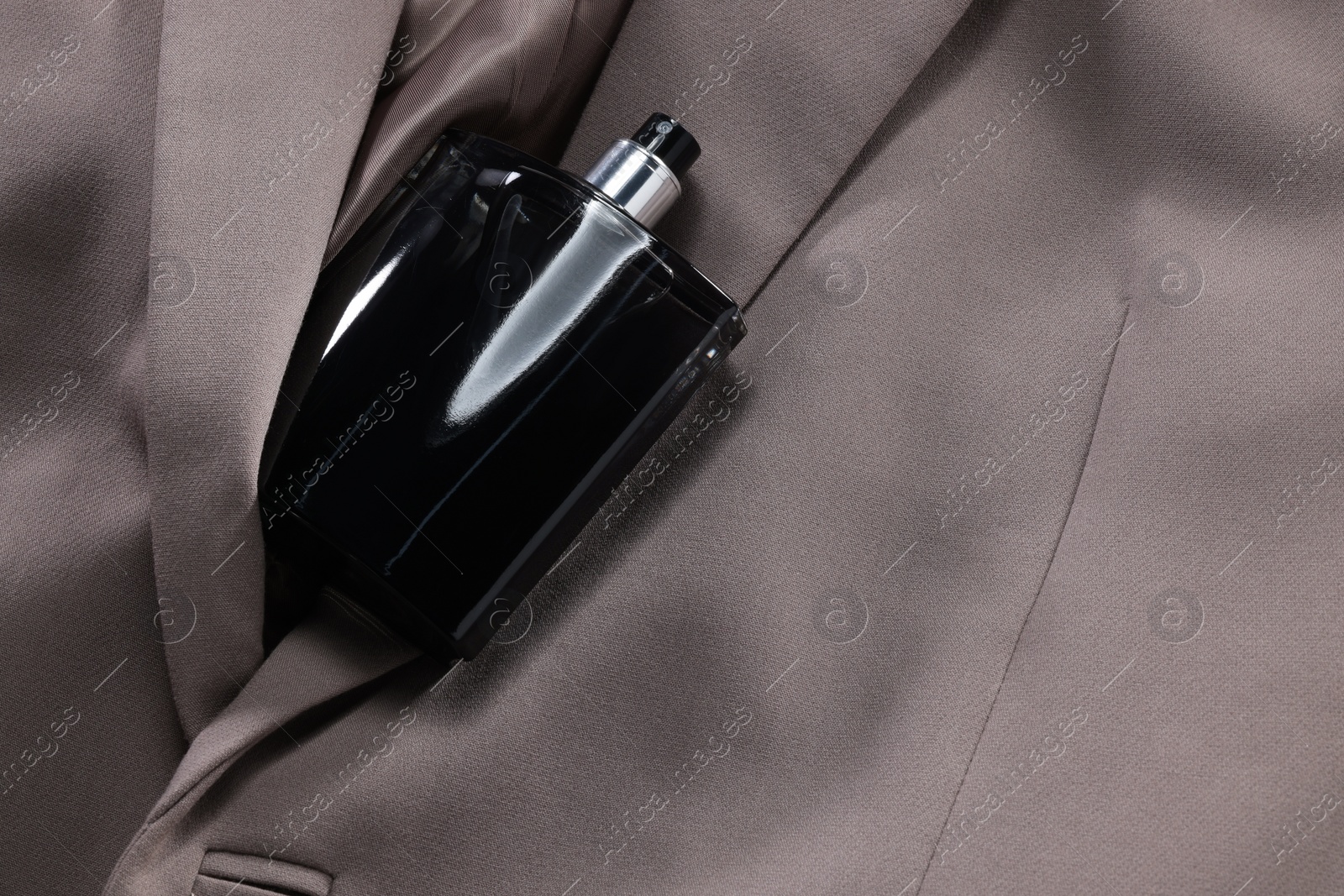 Photo of Luxury men's perfume in bottle on beige jacket, top view. Space for text