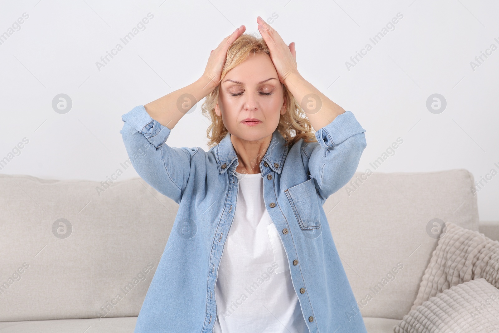 Photo of Woman suffering from headache on sofa indoors. Hormonal disorders