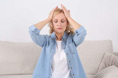 Photo of Woman suffering from headache on sofa indoors. Hormonal disorders