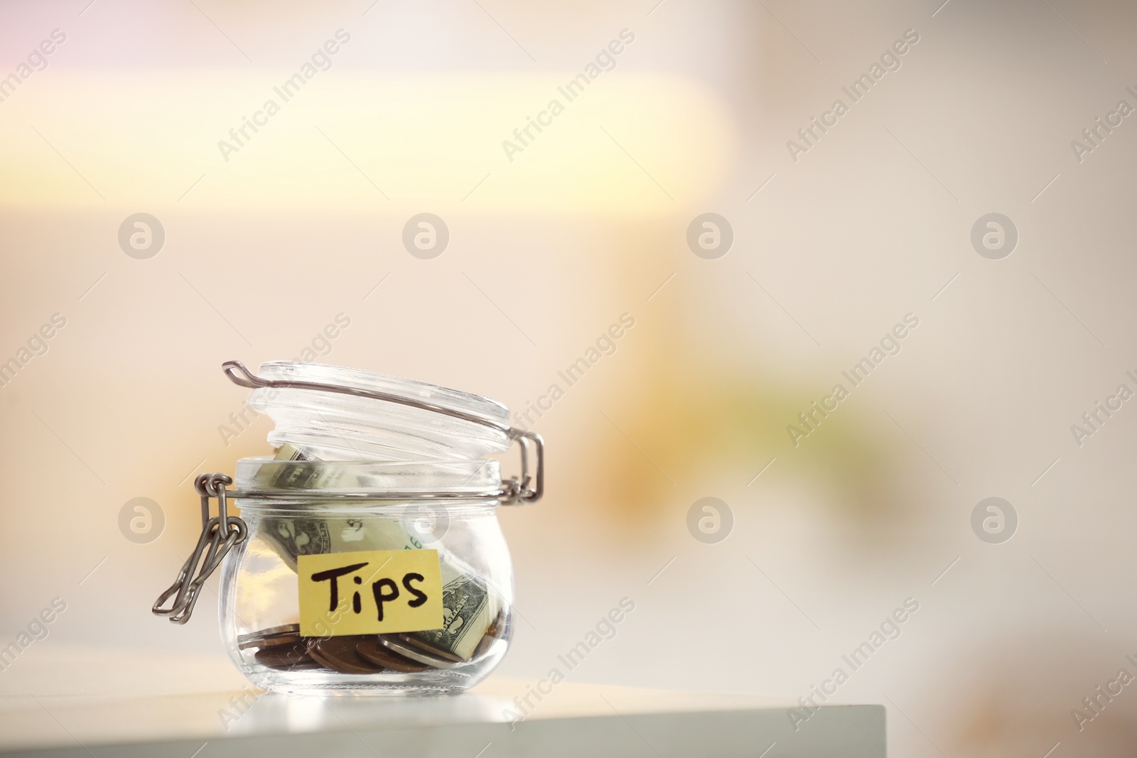 Photo of Tip jar with money on table against blurred background, space for text