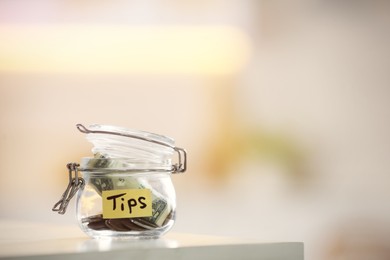 Photo of Tip jar with money on table against blurred background, space for text