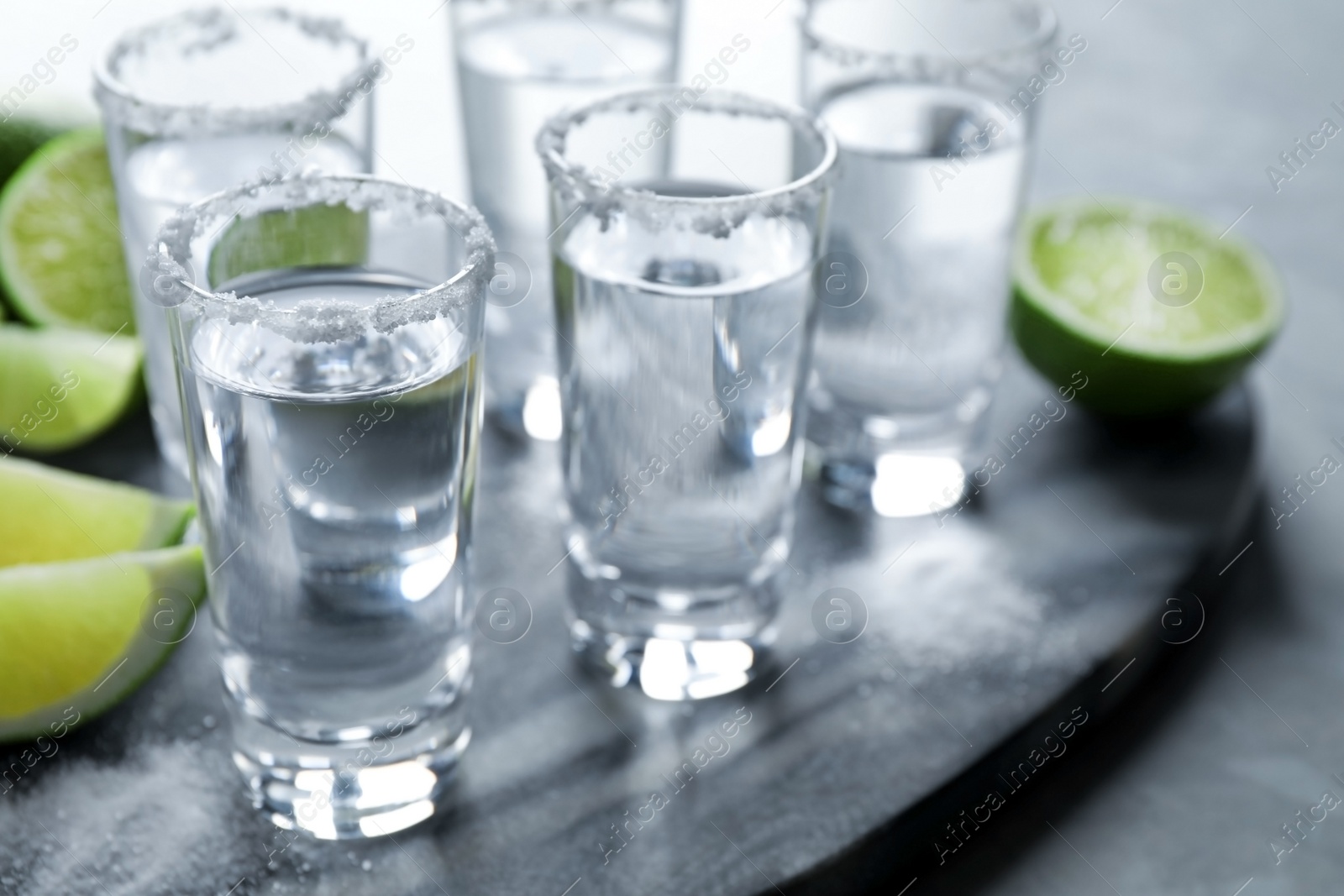 Photo of Mexican Tequila shots, lime slices and salt on grey marble table