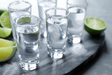 Photo of Mexican Tequila shots, lime slices and salt on grey marble table