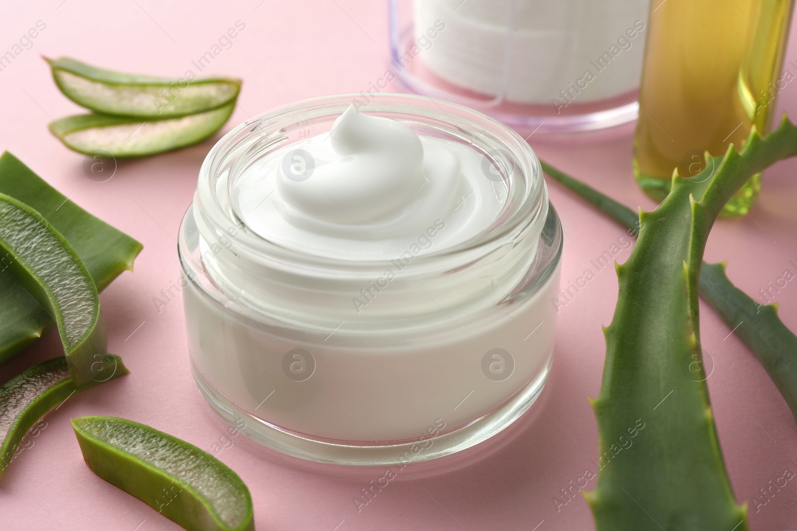 Photo of Jar with cream and cut aloe leaves on pink background, closeup