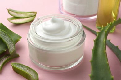Jar with cream and cut aloe leaves on pink background, closeup