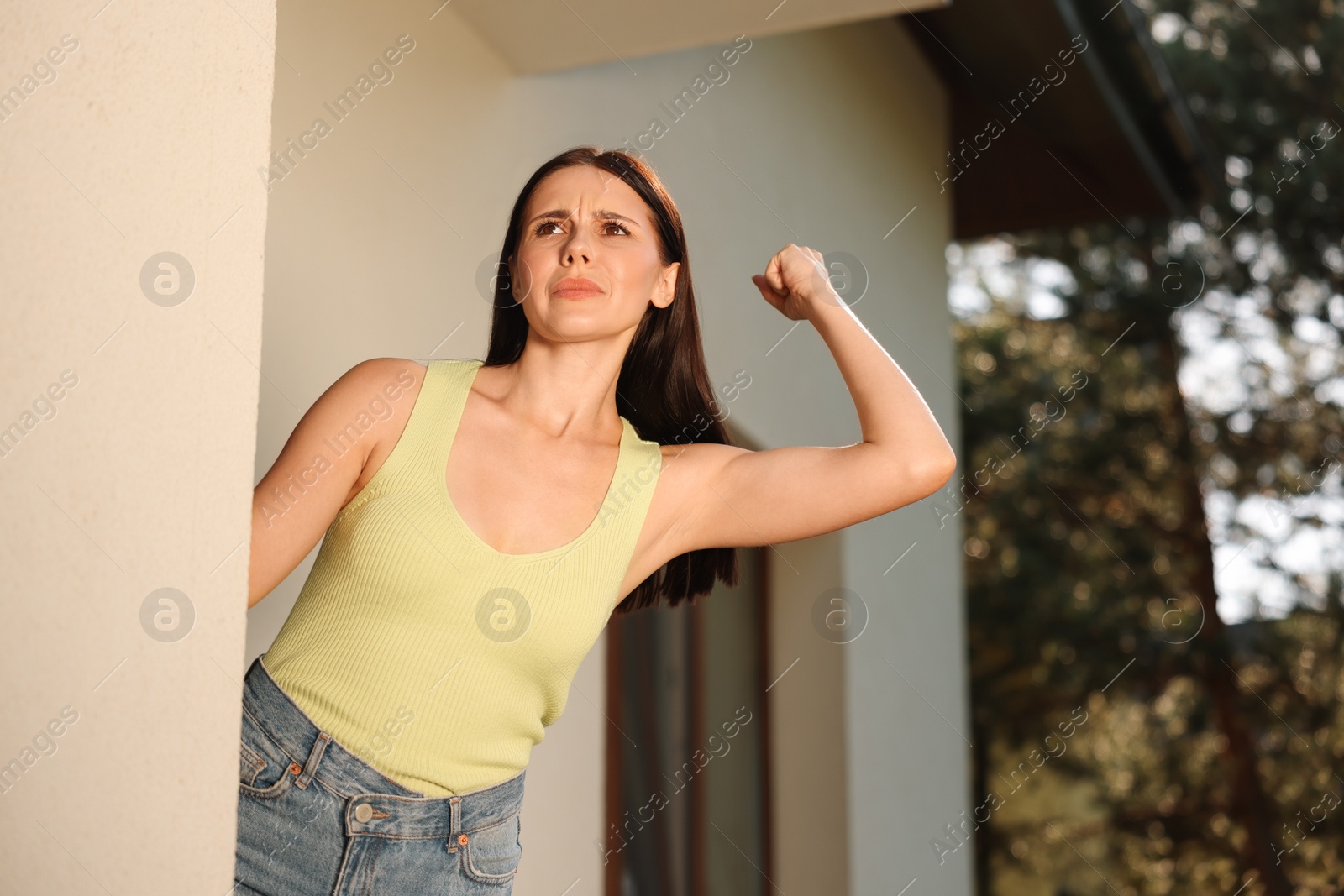 Photo of Angry woman showing fist near house, low angle view. Annoying neighbour