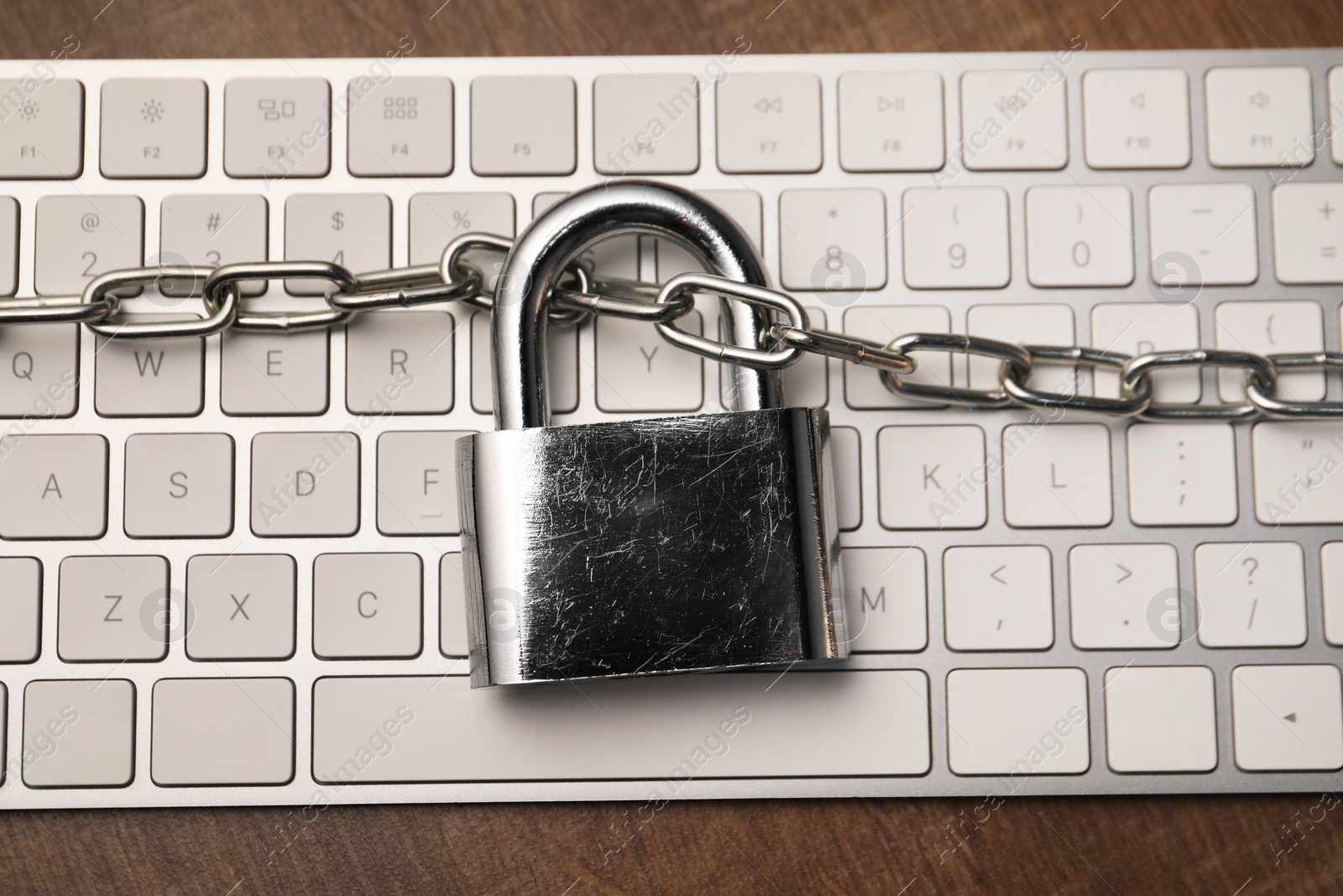 Photo of Cyber security. Keyboard with padlock and chain on wooden table, top view