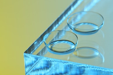 Pair of contact lenses on glass against color background, closeup. Space for text