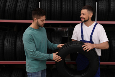 Photo of Mechanic helping client to choose car tire in auto store