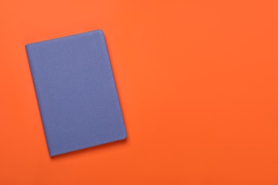 Closed blue notebook on orange background, top view. Space for text