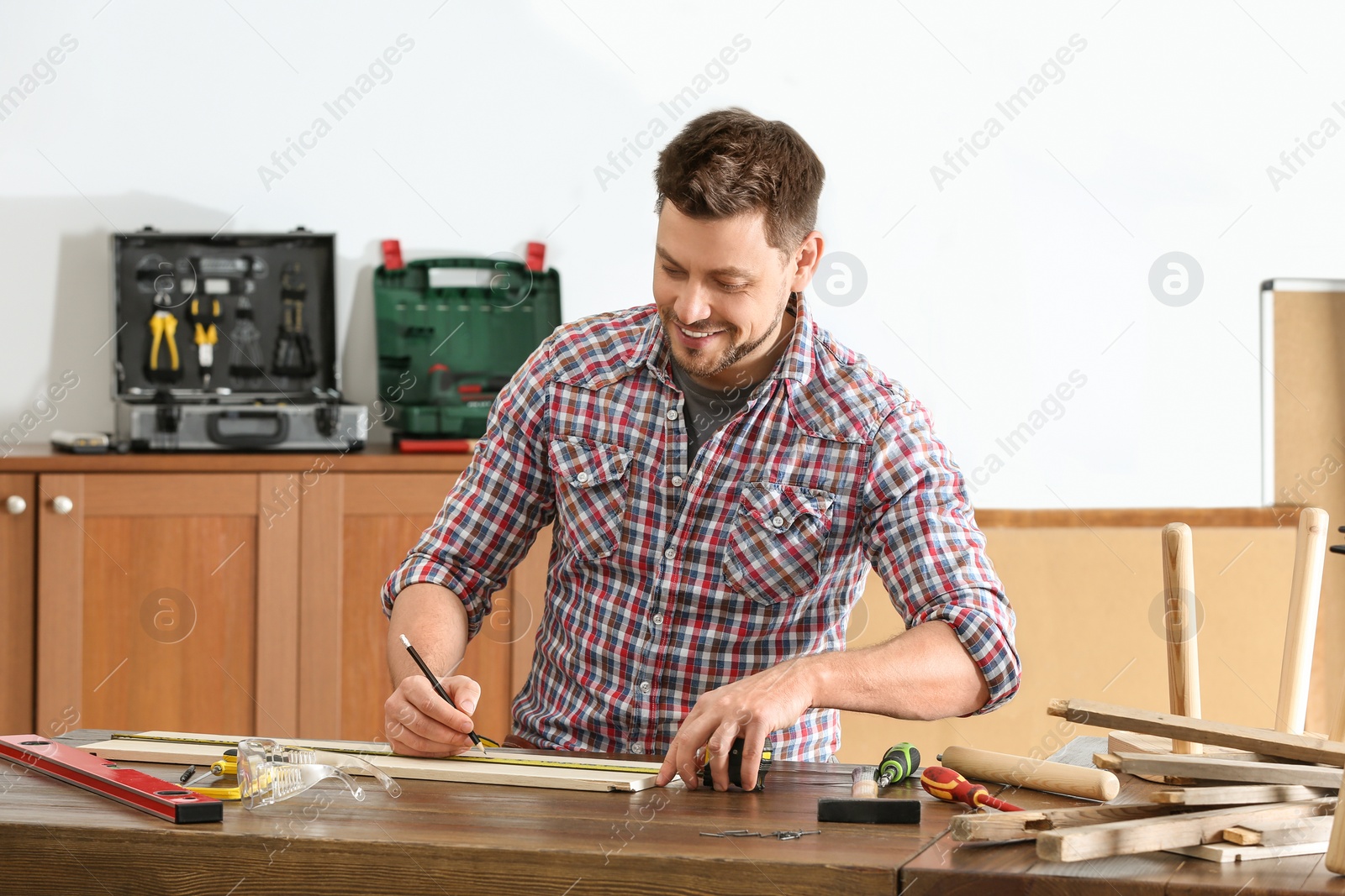 Photo of Handsome working man making marks on timber at table indoors. Home repair