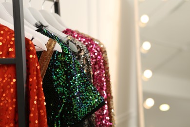 Photo of Clothing rack with colorful sequin party dresses on hangers in boutique, closeup. Space for text